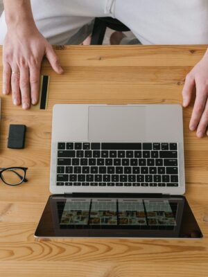 Hands on a laptop, surrounded by gadgets, on a wooden desk. Ideal for online shopping themes.