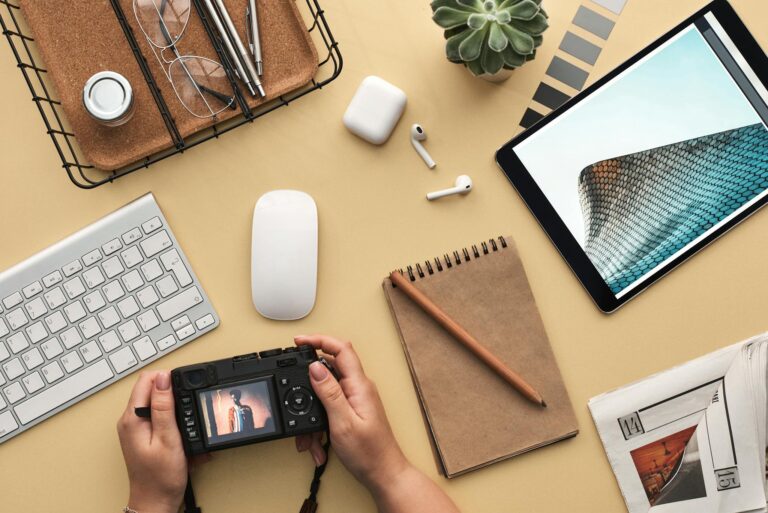 Overhead view of a modern workspace featuring tech gadgets, a camera, and a notepad.