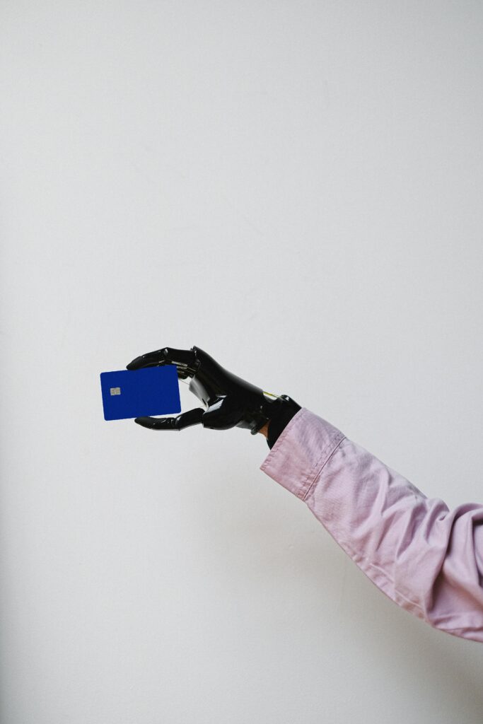 A prosthetic hand in a pink shirt holding a blue card against a white backdrop, showcasing technology and modern design.